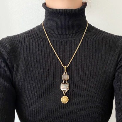 A lavaliere necklace featuring beautifully banded brown and white agate, paired with a gold-tone charm. ブラウンとホワイトの縞模様が美しいメノウと、ゴールドトーンのチャームが組み合わされたラヴァリエネックレス。
