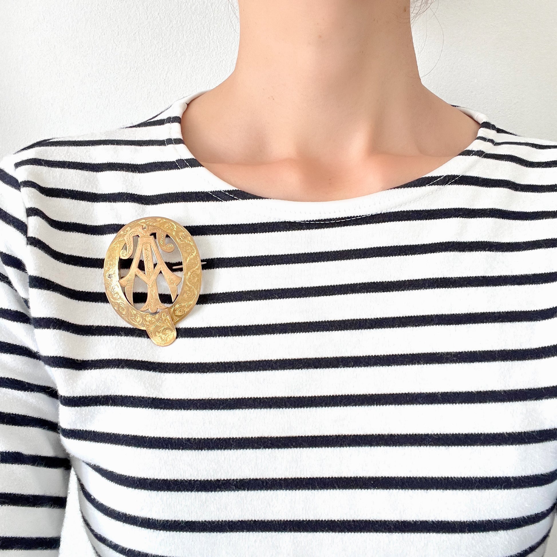 A gold-tone monogram brooch beautifully engraved with a delicate botanical motif.  美しい植物モチーフが彫られたゴールドトーンのモノグラムブローチ。