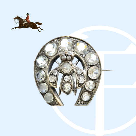 A clear glass brooch featuring a horseshoe motif adorned with a small insect detail. 馬蹄モチーフに、小さな虫があしらわれたクリアグラスのブローチ。