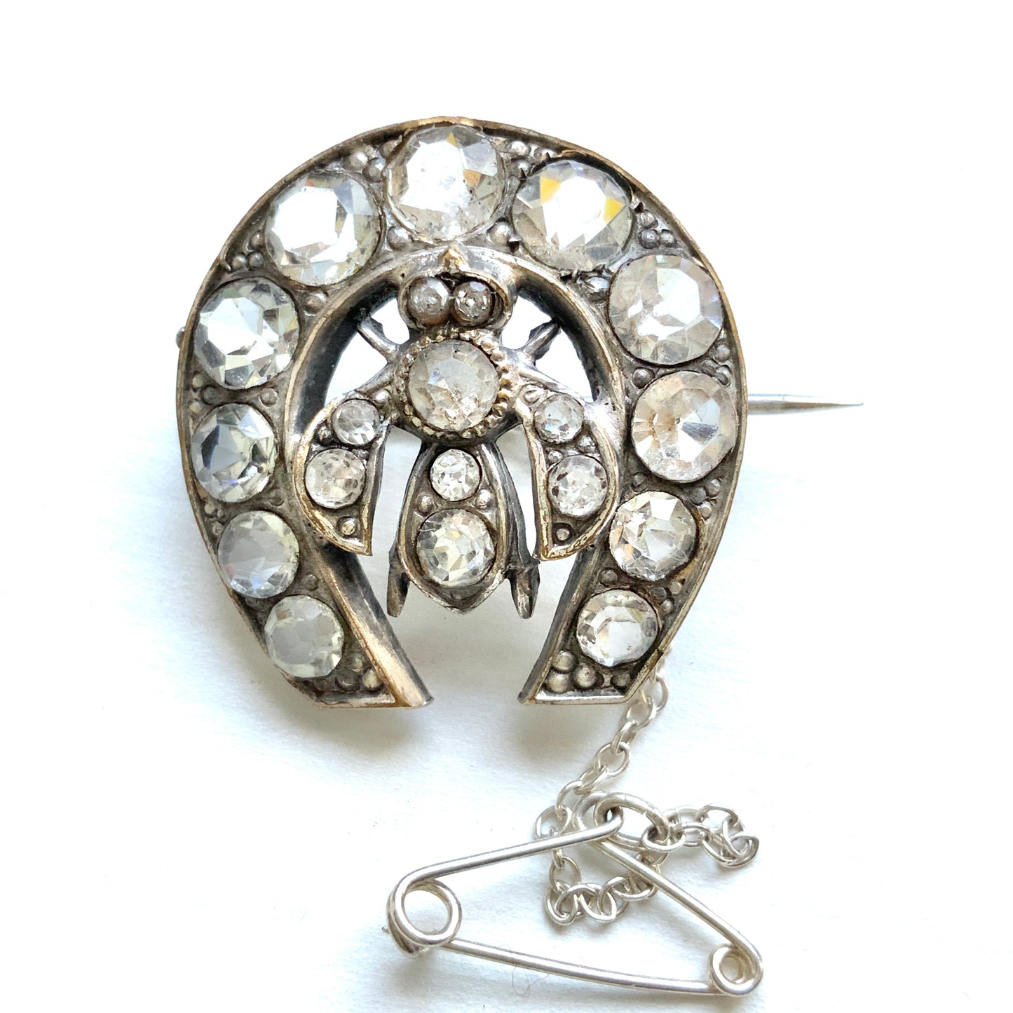 A clear glass brooch featuring a horseshoe motif adorned with a small insect detail. 馬蹄モチーフに、小さな虫があしらわれたクリアグラスのブローチ。