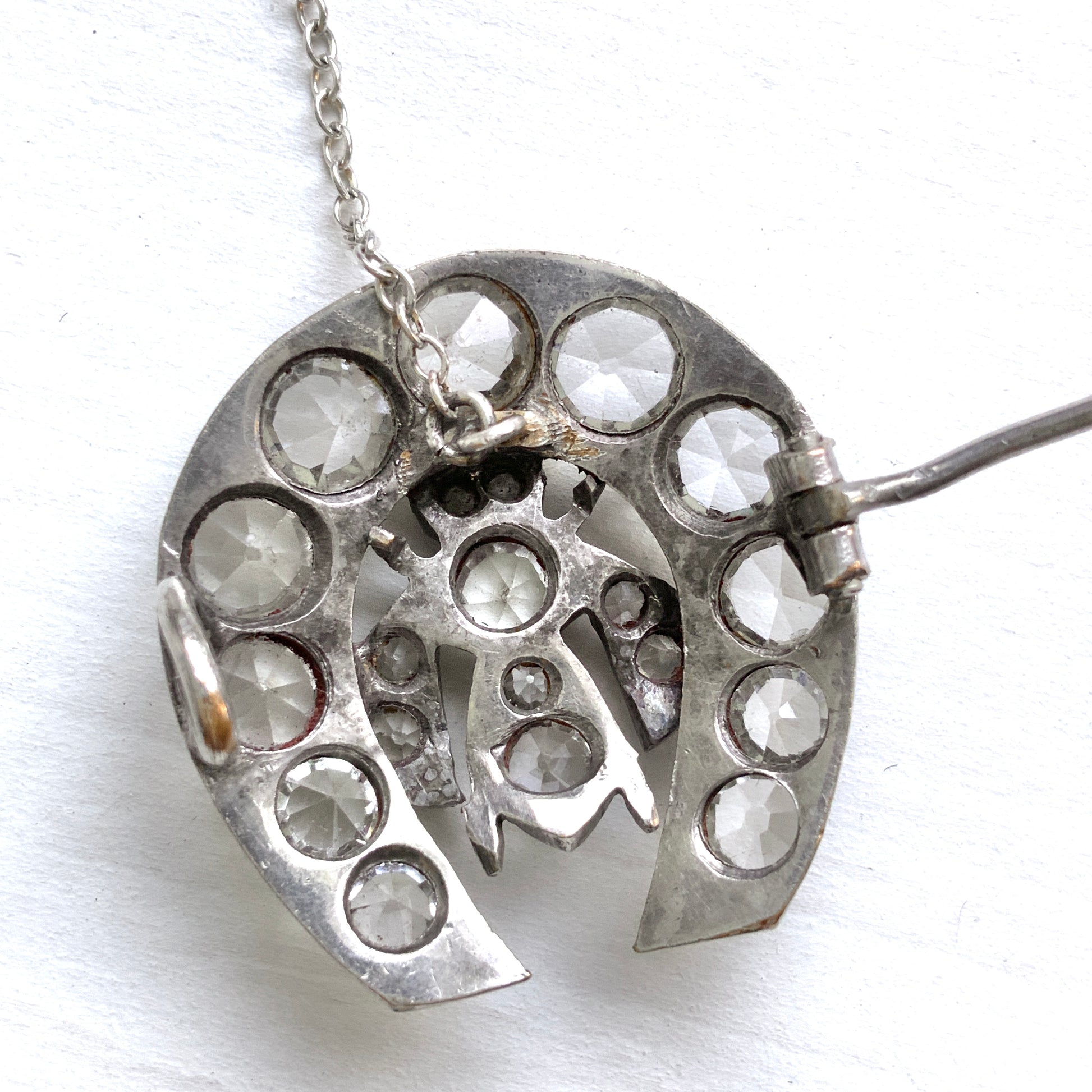 A clear glass brooch featuring a horseshoe motif adorned with a small insect detail. 馬蹄モチーフに、小さな虫があしらわれたクリアグラスのブローチ。