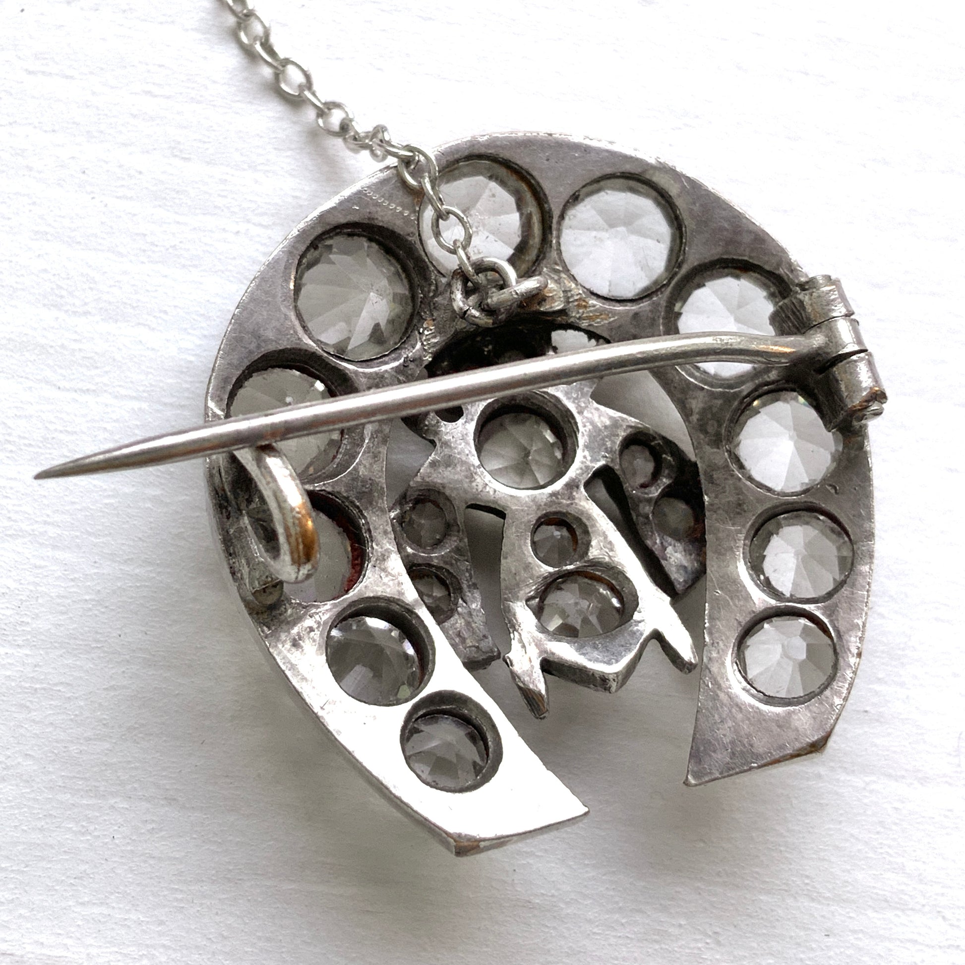 A clear glass brooch featuring a horseshoe motif adorned with a small insect detail. 馬蹄モチーフに、小さな虫があしらわれたクリアグラスのブローチ。