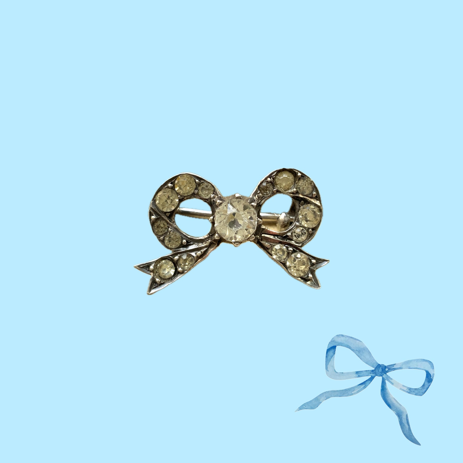 A small silver bow brooch set with rhinestones. ラインストーンがあしらわれた小さなリボンのシルバーブローチ。