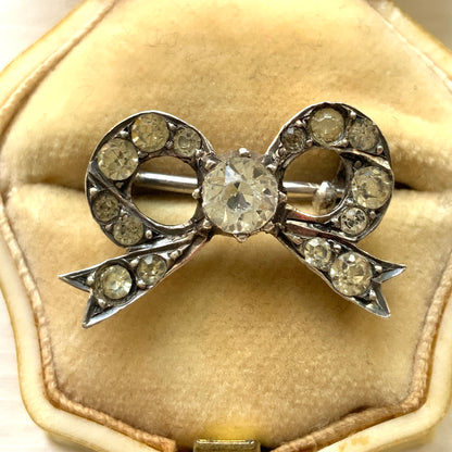 A small silver bow brooch set with rhinestones. ラインストーンがあしらわれた小さなリボンのシルバーブローチ。