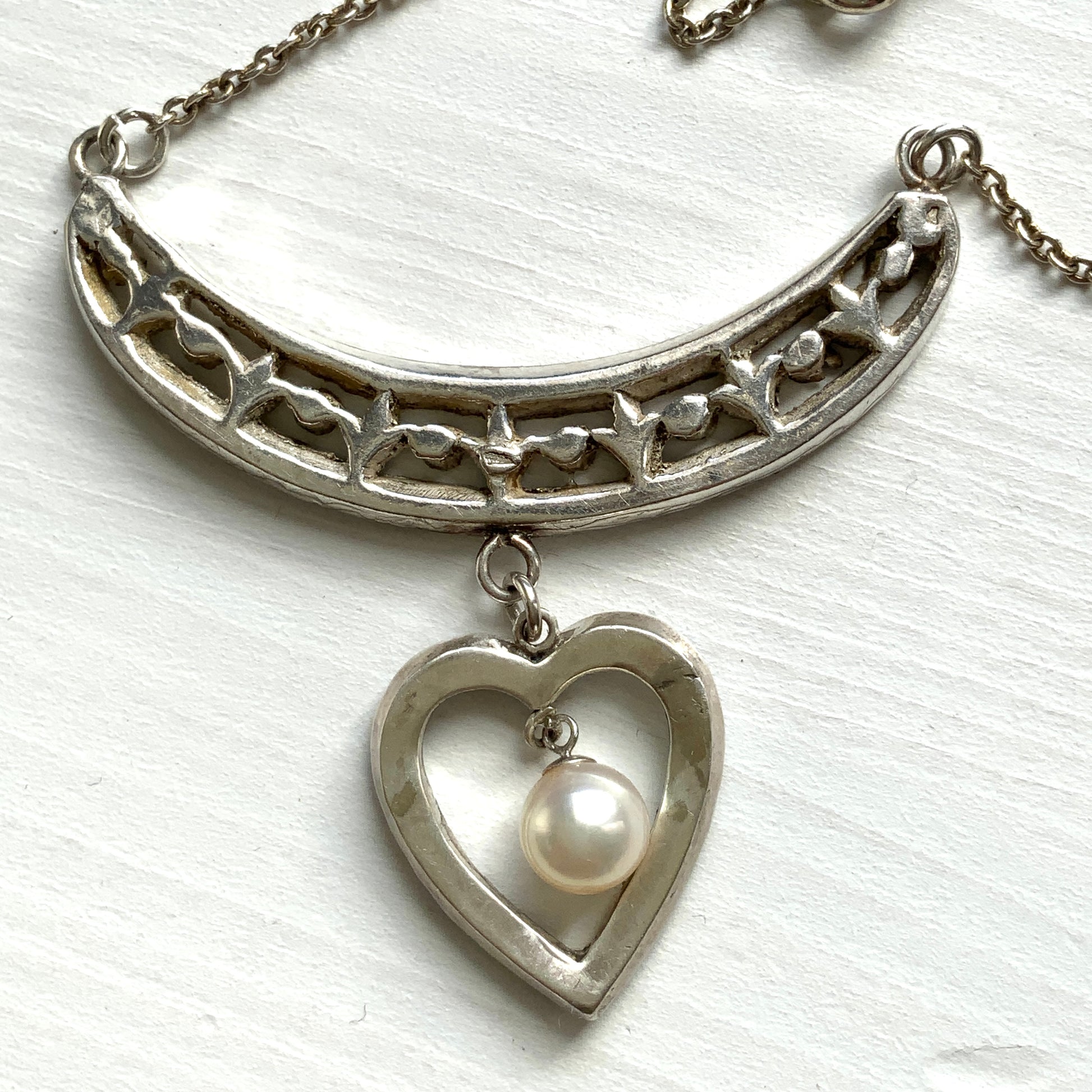 A silver pendant necklace featuring a crescent bar and heart motif.  クレセントバーとハートモチーフのシルバーペンダントネックレス。 