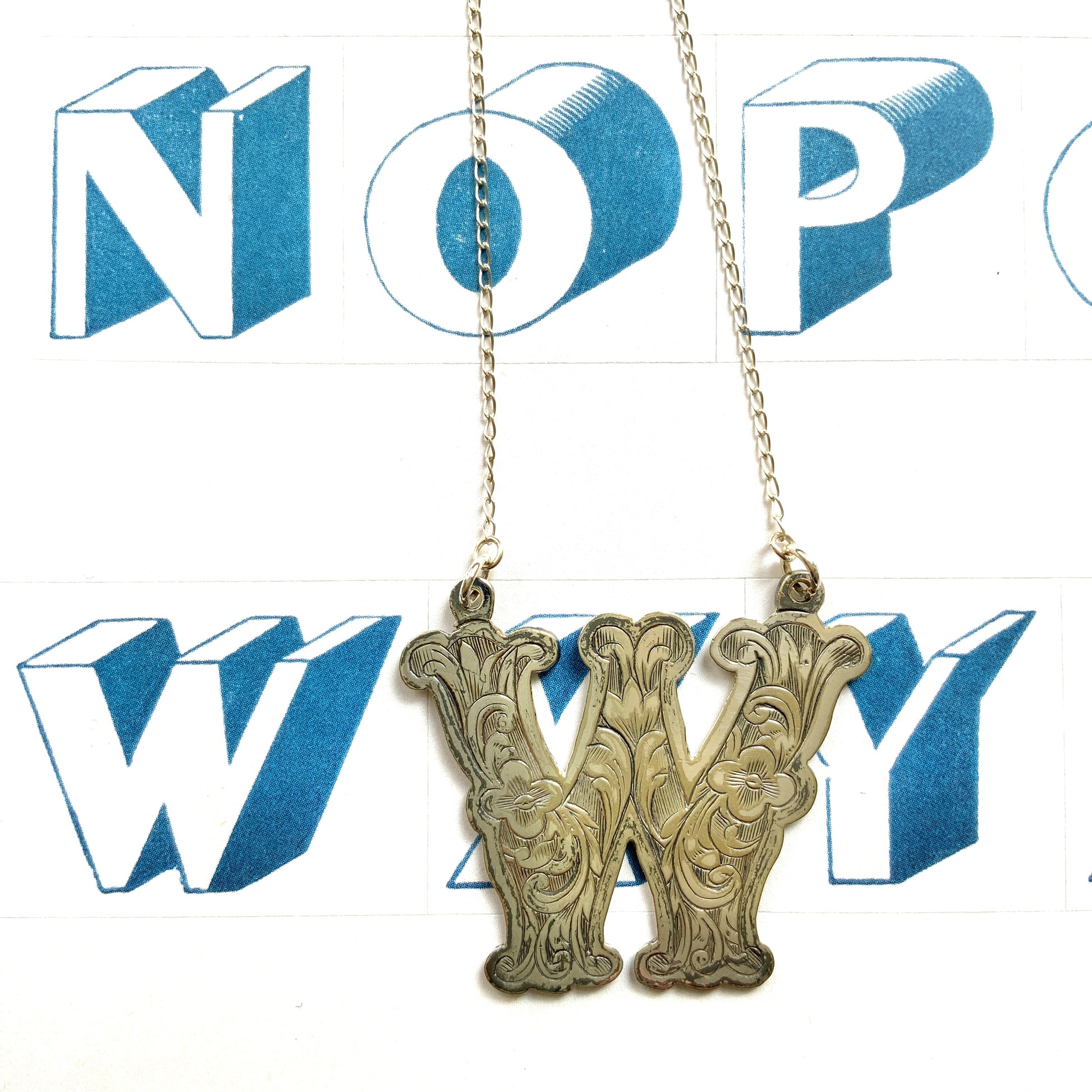 A necklace featuring the letter “W”, beautifully engraved with a botanical motif. 美しい植物モチーフのエングレービングが施された“W”のネックレス。 