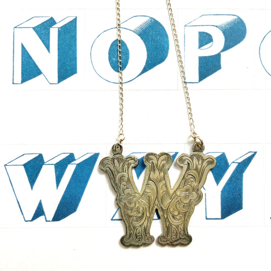 A necklace featuring the letter “W”, beautifully engraved with a botanical motif. 美しい植物モチーフのエングレービングが施された“W”のネックレス。 