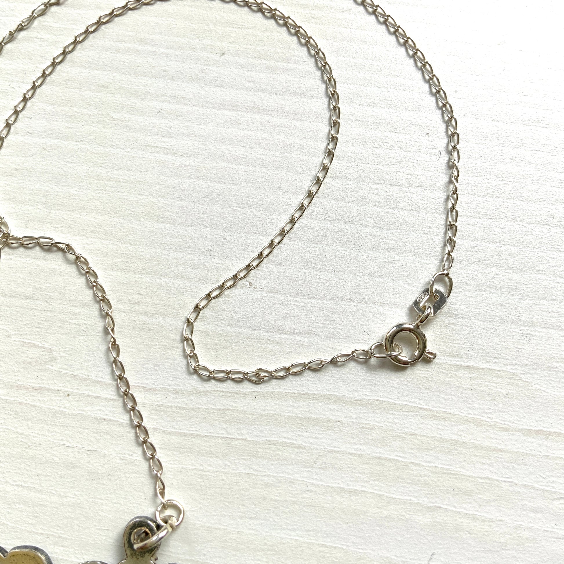 A necklace featuring the letter “W”, beautifully engraved with a botanical motif. 美しい植物モチーフのエングレービングが施された“W”のネックレス。 