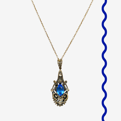 A vintage pendant necklace featuring a vivid blue navette glass stone surrounded by floral motifs. 鮮やかなブルーのナヴェットグラスの周りに、フローラルモチーフがあしらわれたヴィンテージのペンダントネックレス。