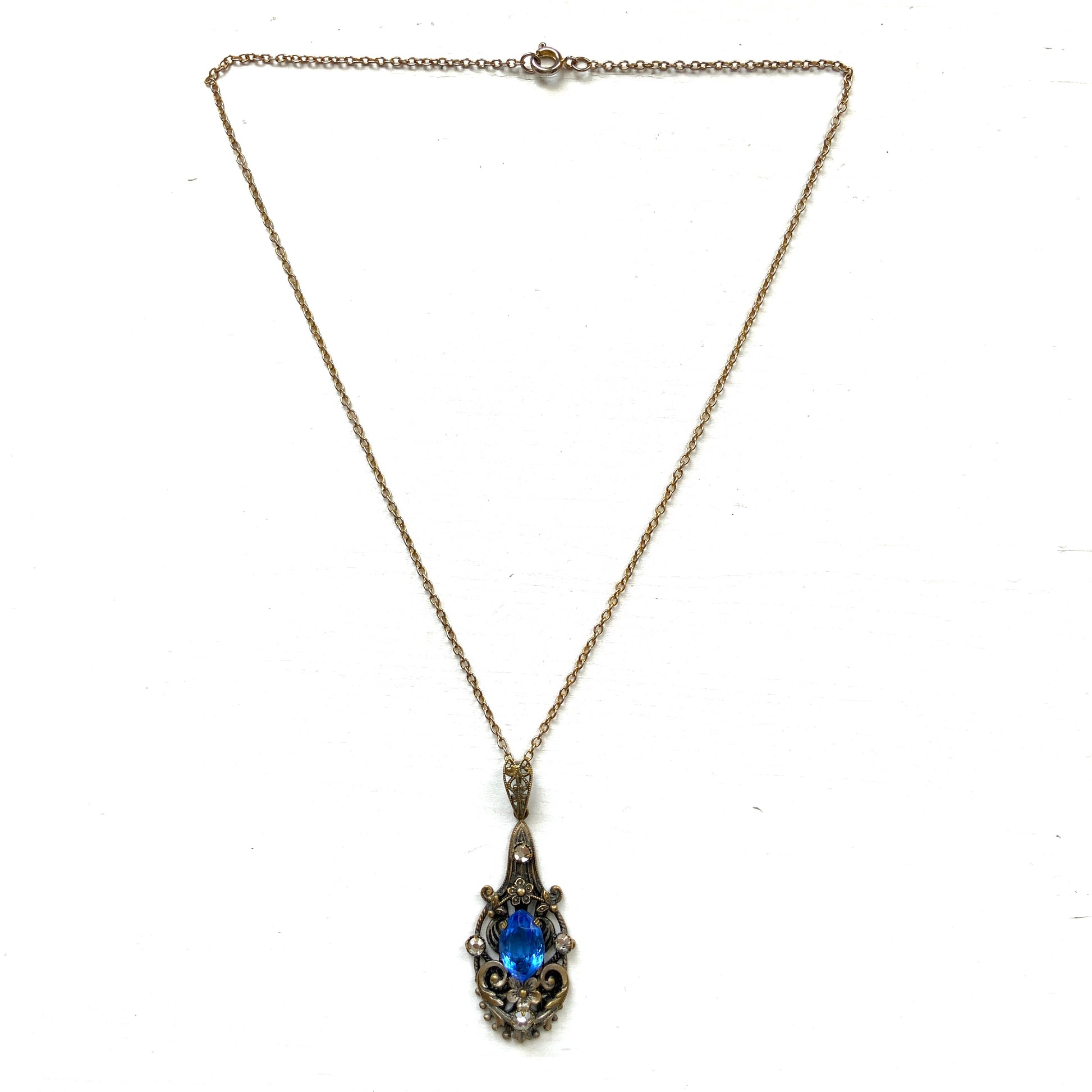 A vintage pendant necklace featuring a vivid blue navette glass stone surrounded by floral motifs. 鮮やかなブルーのナヴェットグラスの周りに、フローラルモチーフがあしらわれたヴィンテージのペンダントネックレス。