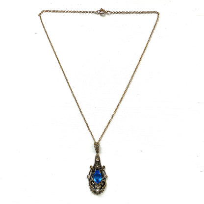 A vintage pendant necklace featuring a vivid blue navette glass stone surrounded by floral motifs. 鮮やかなブルーのナヴェットグラスの周りに、フローラルモチーフがあしらわれたヴィンテージのペンダントネックレス。