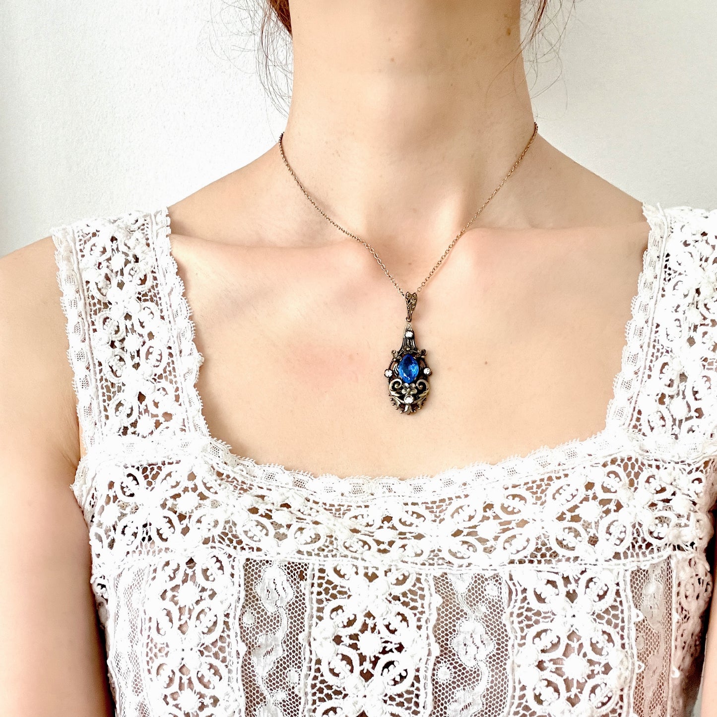 A vintage pendant necklace featuring a vivid blue navette glass stone surrounded by floral motifs. 鮮やかなブルーのナヴェットグラスの周りに、フローラルモチーフがあしらわれたヴィンテージのペンダントネックレス。