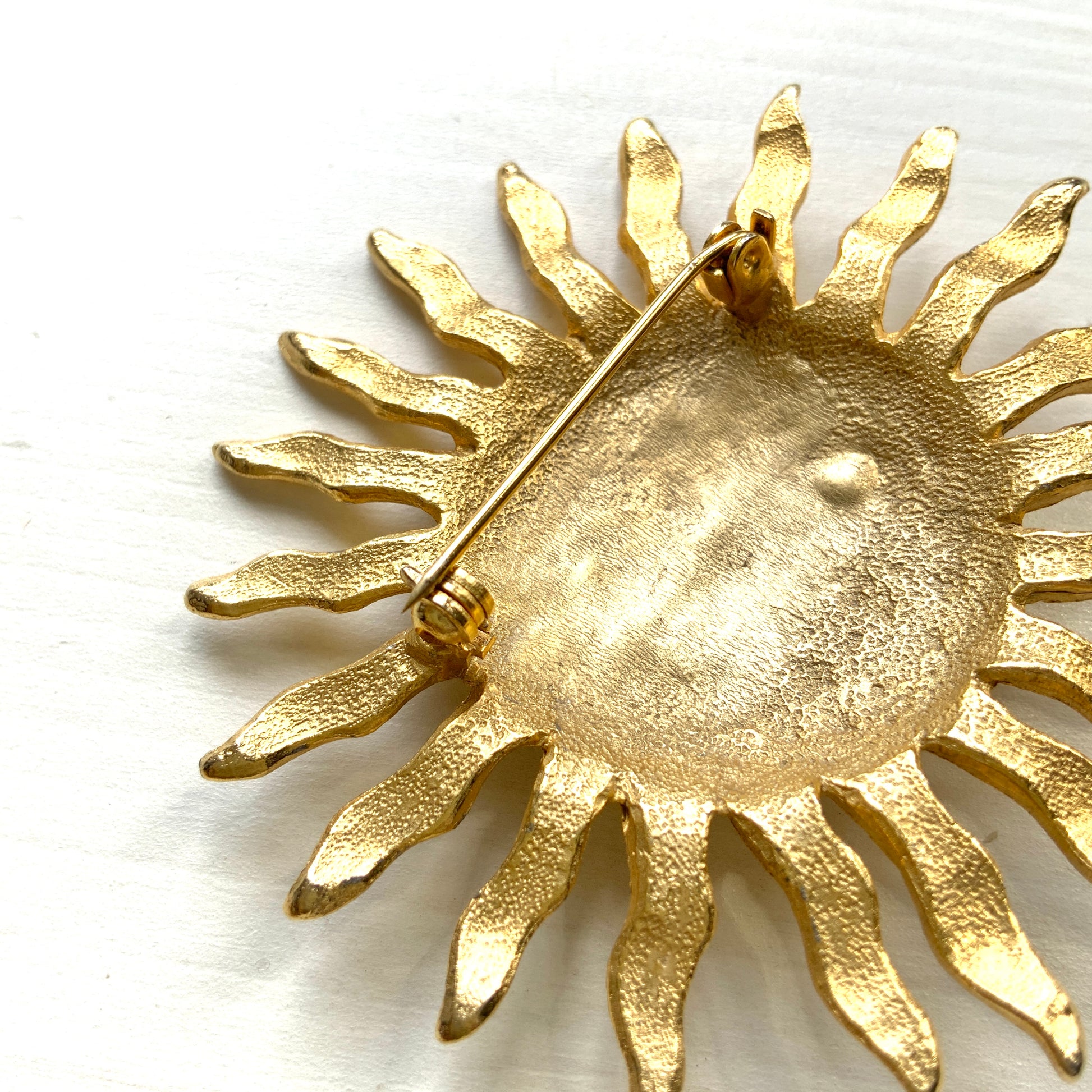 A charming vintage sun brooch featuring a smiling face.  笑顔をたたえた太陽のヴィンテージブローチ。