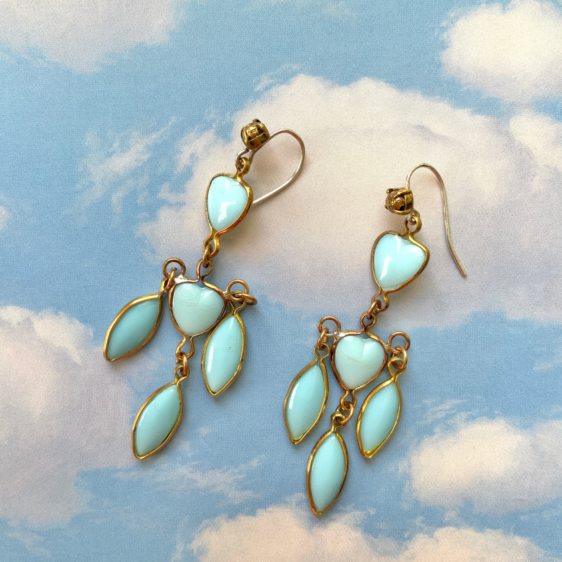 A pair of earrings featuring a pale turquoise heart glass chain adorned with marquise-shaped glass fringe. 淡いターコイズカラーのハートグラスチェーンに、マーキス 型のグラスのフリンジがついたピアス。 