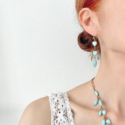 A pair of earrings featuring a pale turquoise heart glass chain adorned with marquise-shaped glass fringe. 淡いターコイズカラーのハートグラスチェーンに、マーキス 型のグラスのフリンジがついたピアス。 
