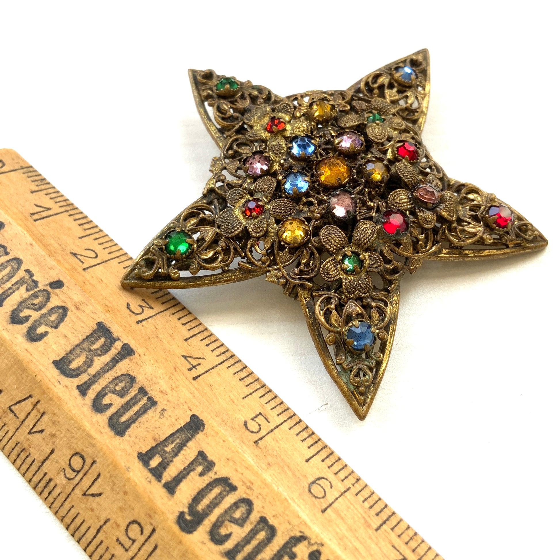 A beautiful vintage brooch featuring a star-shaped design crafted in intricate gold-tone filigree, adorned with multicoloured rhinestones. ゴールドトーンの繊細なフィリグリー細工でかたどられた星に、色とりどりのラインストーンがあしらわれたヴィンテージブローチ。 