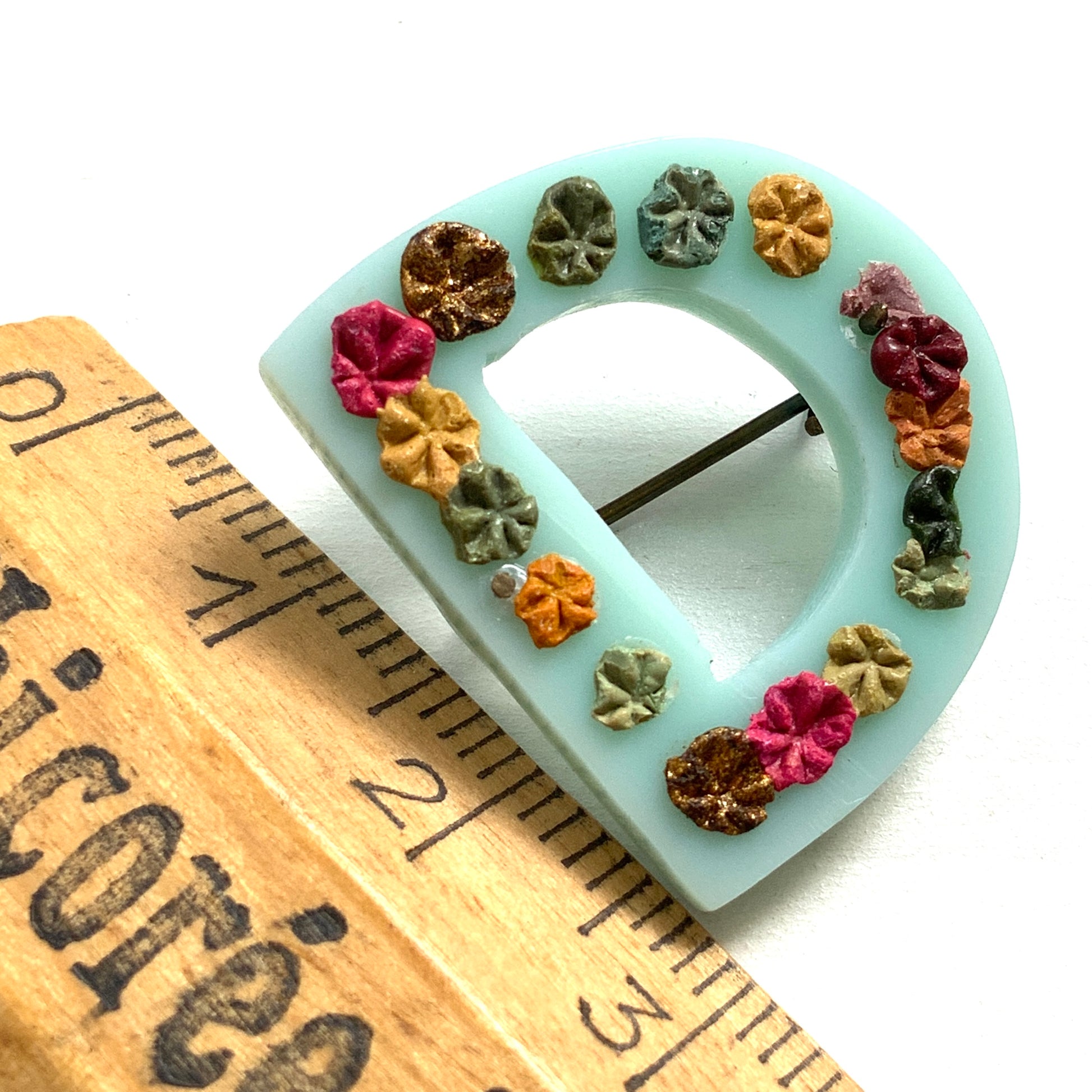 A brooch in the shape of the letter “D”, crafted from pale blue early plastic and adorned with colourful clay flowers. 淡い水色のアーリープラスチックに、カラフルなクレイのお花が咲いた”D"のブローチ。