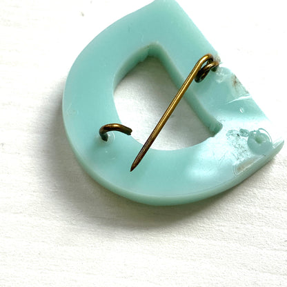 A brooch in the shape of the letter “D”, crafted from pale blue early plastic and adorned with colourful clay flowers. 淡い水色のアーリープラスチックに、カラフルなクレイのお花が咲いた”D"のブローチ。