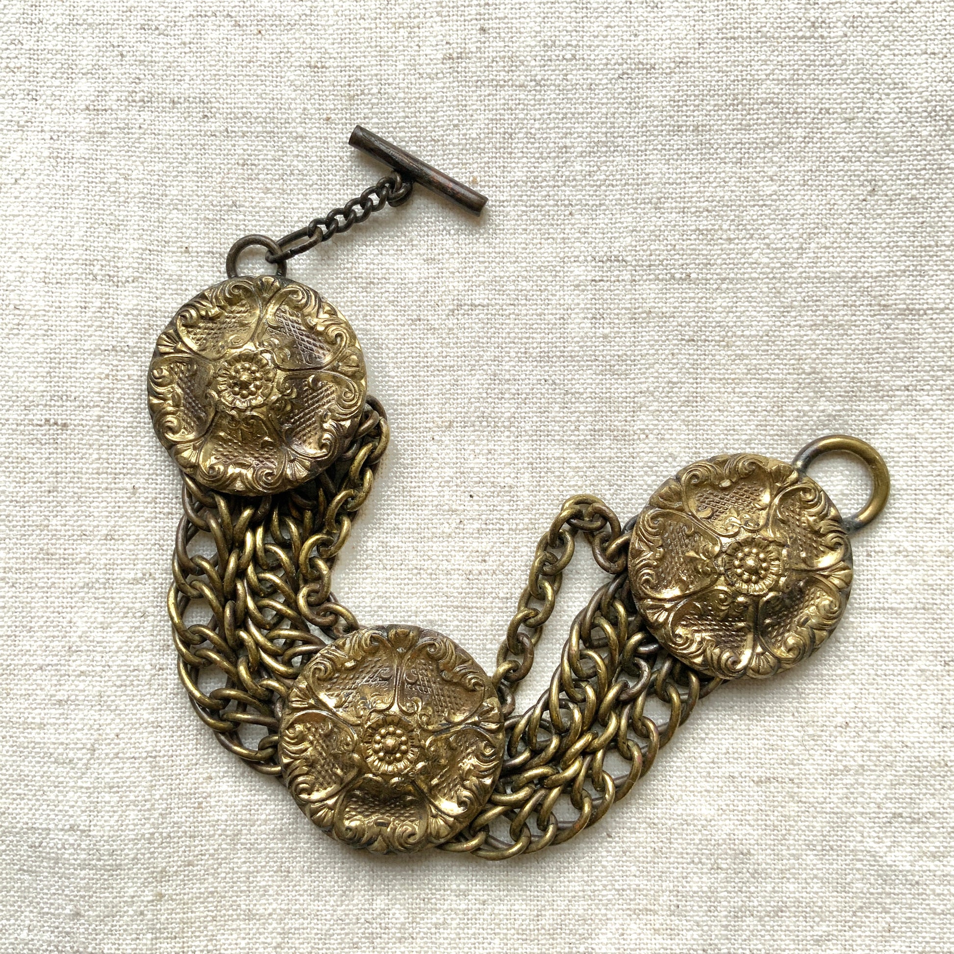 Brass bracelet featuring ornate floral discs linked with multiple chains. フローラルモチーフのメタルディスクと多連チェーンを組み合わせた、ブラス製ブレスレット。 