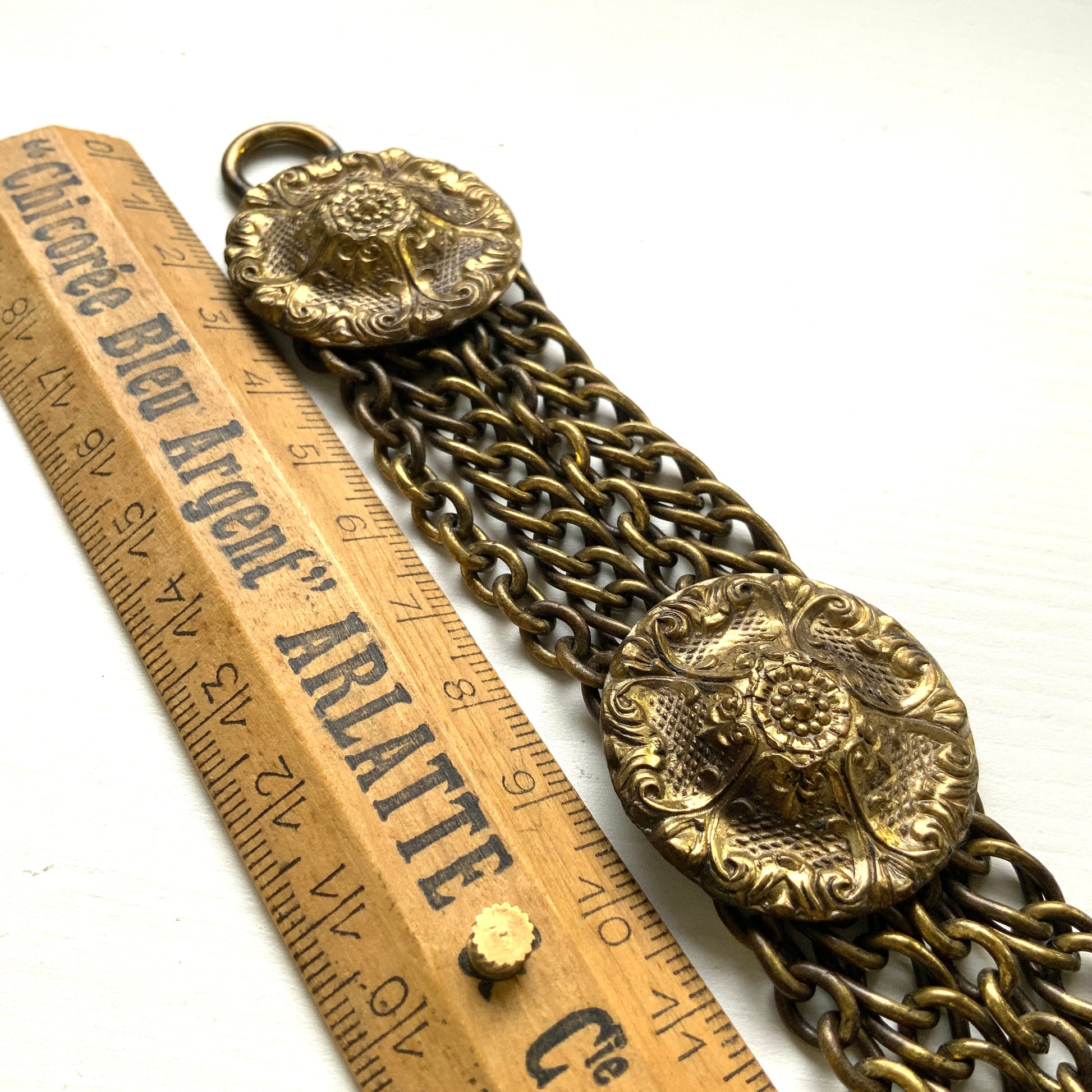 Brass bracelet featuring ornate floral discs linked with multiple chains. フローラルモチーフのメタルディスクと多連チェーンを組み合わせた、ブラス製ブレスレット。 