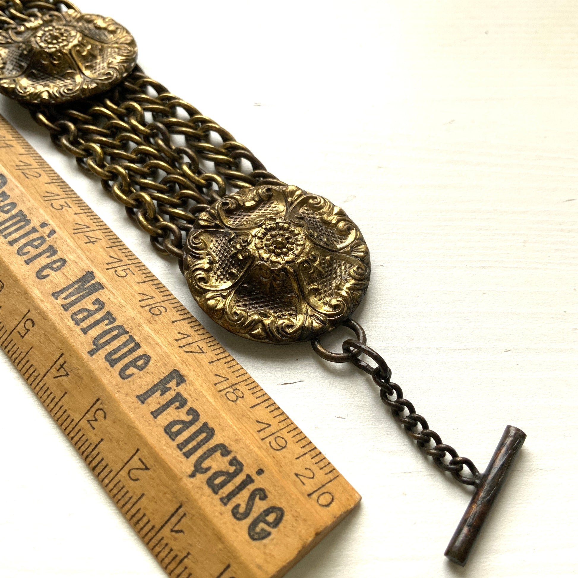 Brass bracelet featuring ornate floral discs linked with multiple chains. フローラルモチーフのメタルディスクと多連チェーンを組み合わせた、ブラス製ブレスレット。 