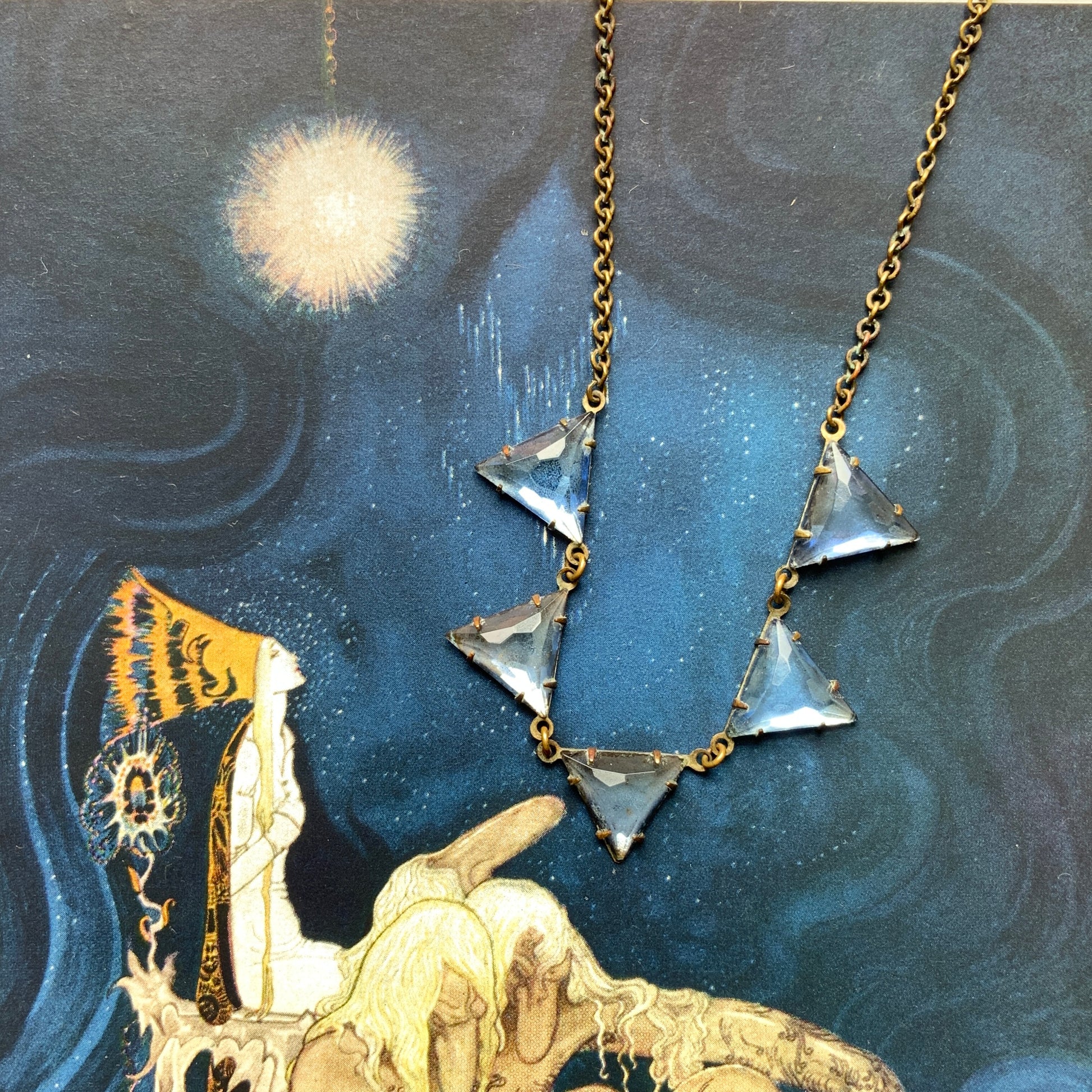 A necklace featuring blue, triangle-shaped mirrored glass, arranged like a string of bunting. ブルーのトライアングル型ミラーグラスが、バンティングのように並んだネックレス。 