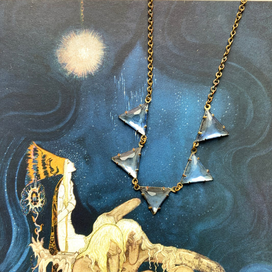 A necklace featuring blue, triangle-shaped mirrored glass, arranged like a string of bunting. ブルーのトライアングル型ミラーグラスが、バンティングのように並んだネックレス。 