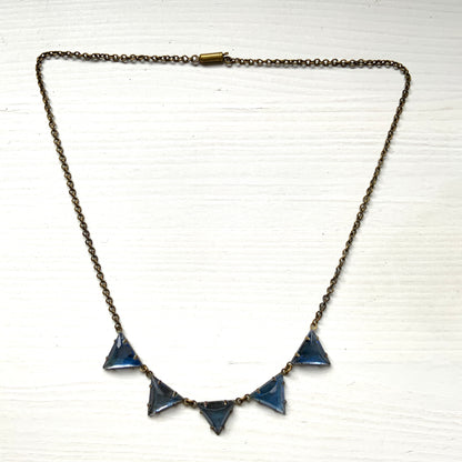 A necklace featuring blue, triangle-shaped mirrored glass, arranged like a string of bunting. ブルーのトライアングル型ミラーグラスが、バンティングのように並んだネックレス。 