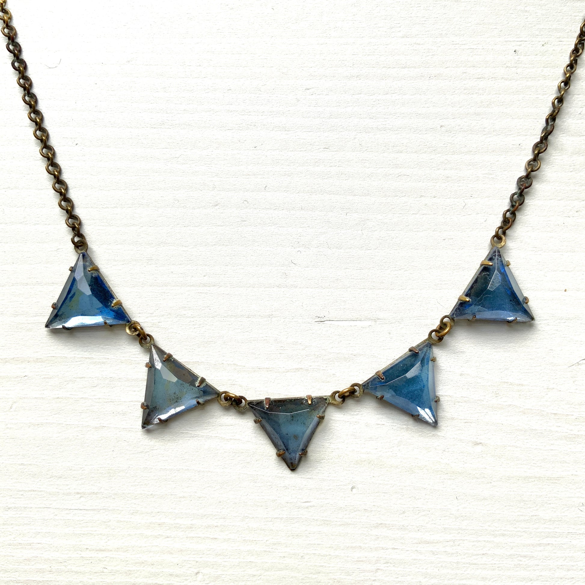 A necklace featuring blue, triangle-shaped mirrored glass, arranged like a string of bunting. ブルーのトライアングル型ミラーグラスが、バンティングのように並んだネックレス。 