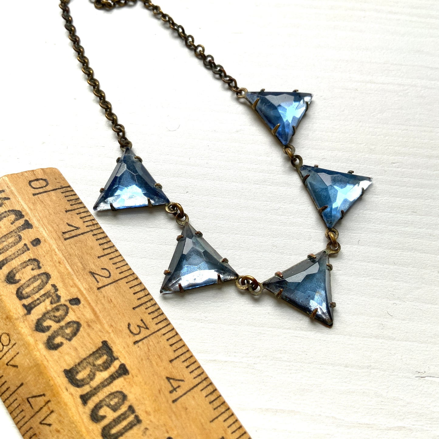 A necklace featuring blue, triangle-shaped mirrored glass, arranged like a string of bunting. ブルーのトライアングル型ミラーグラスが、バンティングのように並んだネックレス。 