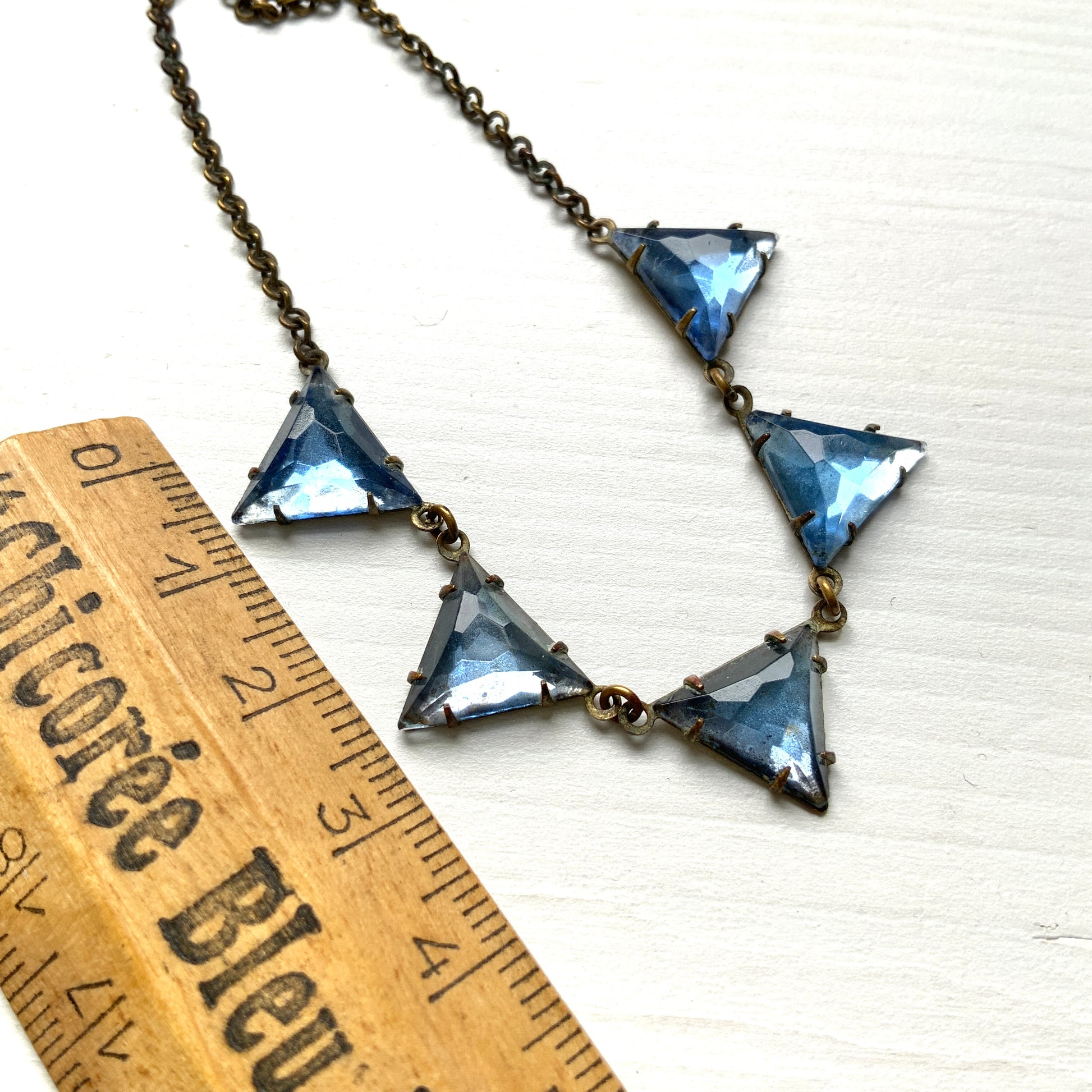 A necklace featuring blue, triangle-shaped mirrored glass, arranged like a string of bunting. ブルーのトライアングル型ミラーグラスが、バンティングのように並んだネックレス。 
