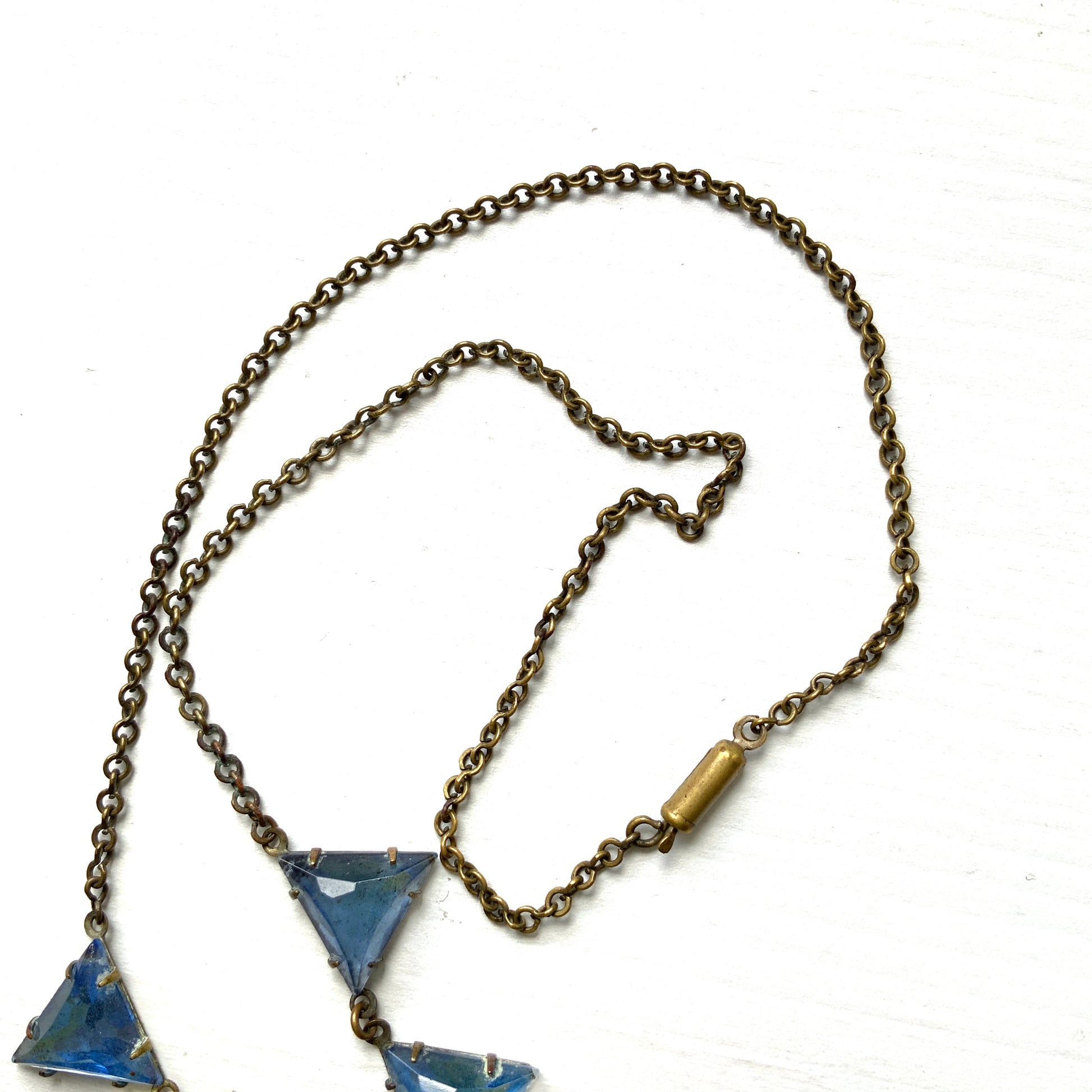 A necklace featuring blue, triangle-shaped mirrored glass, arranged like a string of bunting. ブルーのトライアングル型ミラーグラスが、バンティングのように並んだネックレス。 