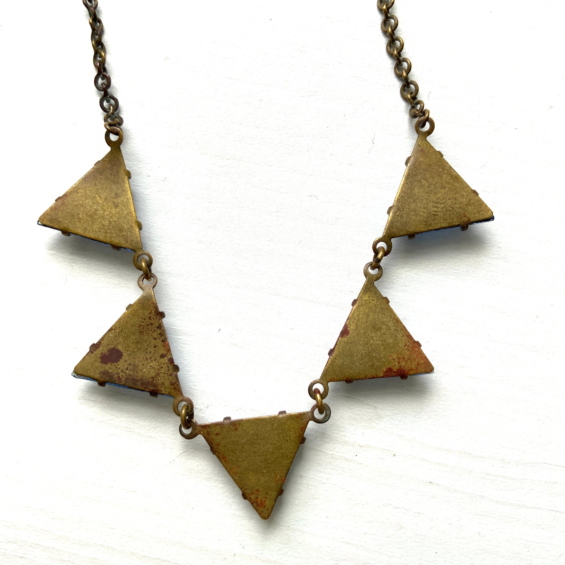 A necklace featuring blue, triangle-shaped mirrored glass, arranged like a string of bunting. ブルーのトライアングル型ミラーグラスが、バンティングのように並んだネックレス。 