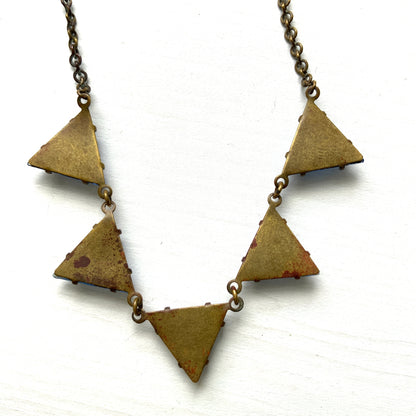 A necklace featuring blue, triangle-shaped mirrored glass, arranged like a string of bunting. ブルーのトライアングル型ミラーグラスが、バンティングのように並んだネックレス。 