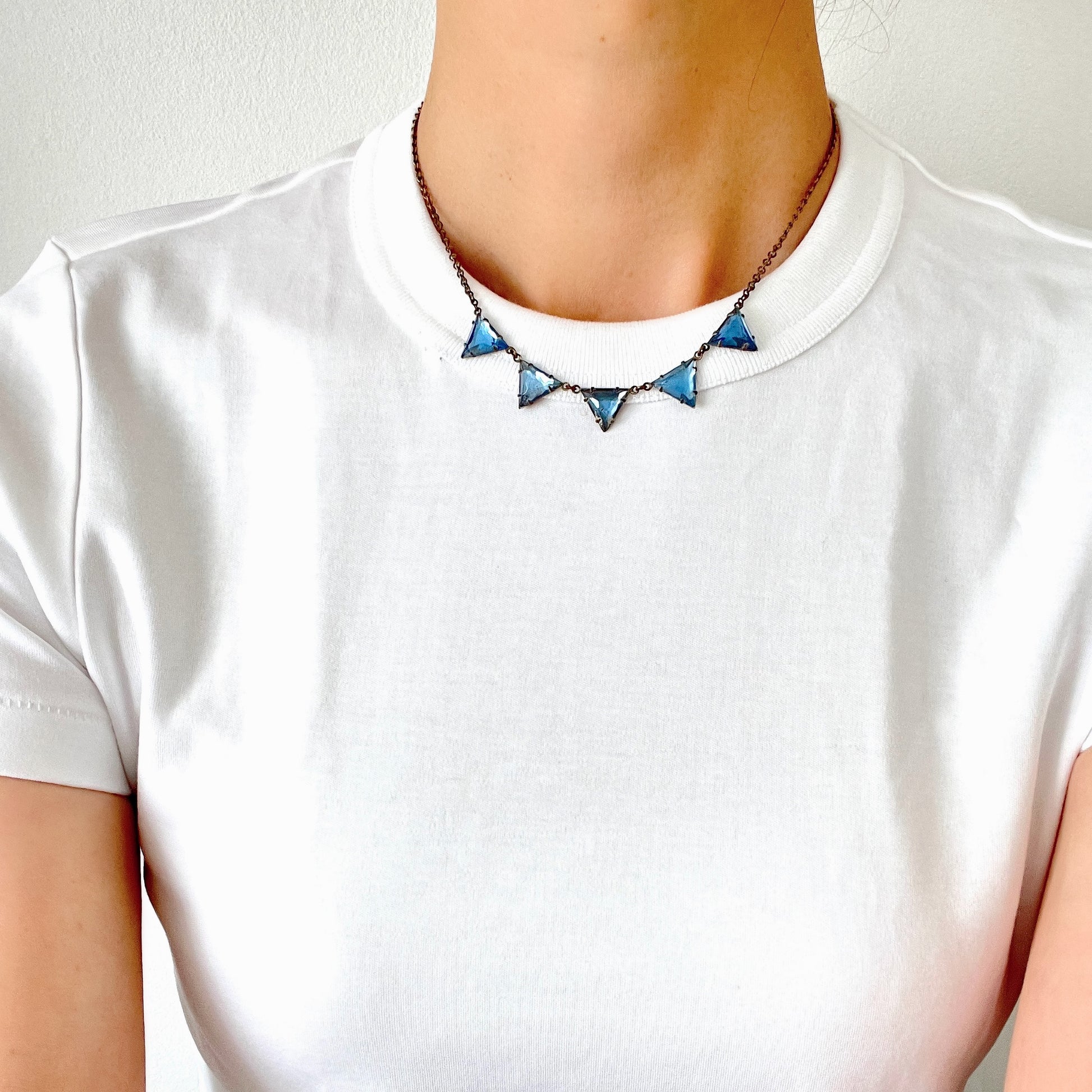 A necklace featuring blue, triangle-shaped mirrored glass, arranged like a string of bunting. ブルーのトライアングル型ミラーグラスが、バンティングのように並んだネックレス。 