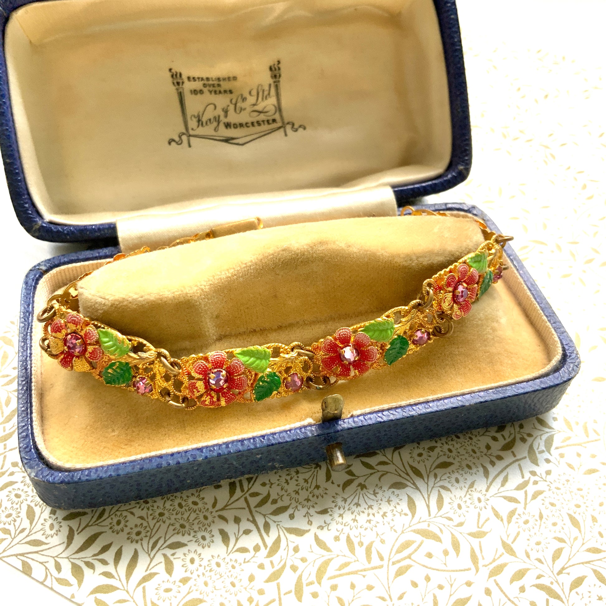 This gold-tone filigree bracelet features charming pink flowers delicately painted onto its dainty filigree plates. かわいらしいピンクのお花が描かれたゴールドトーンのフィリグリーのブレスレット。