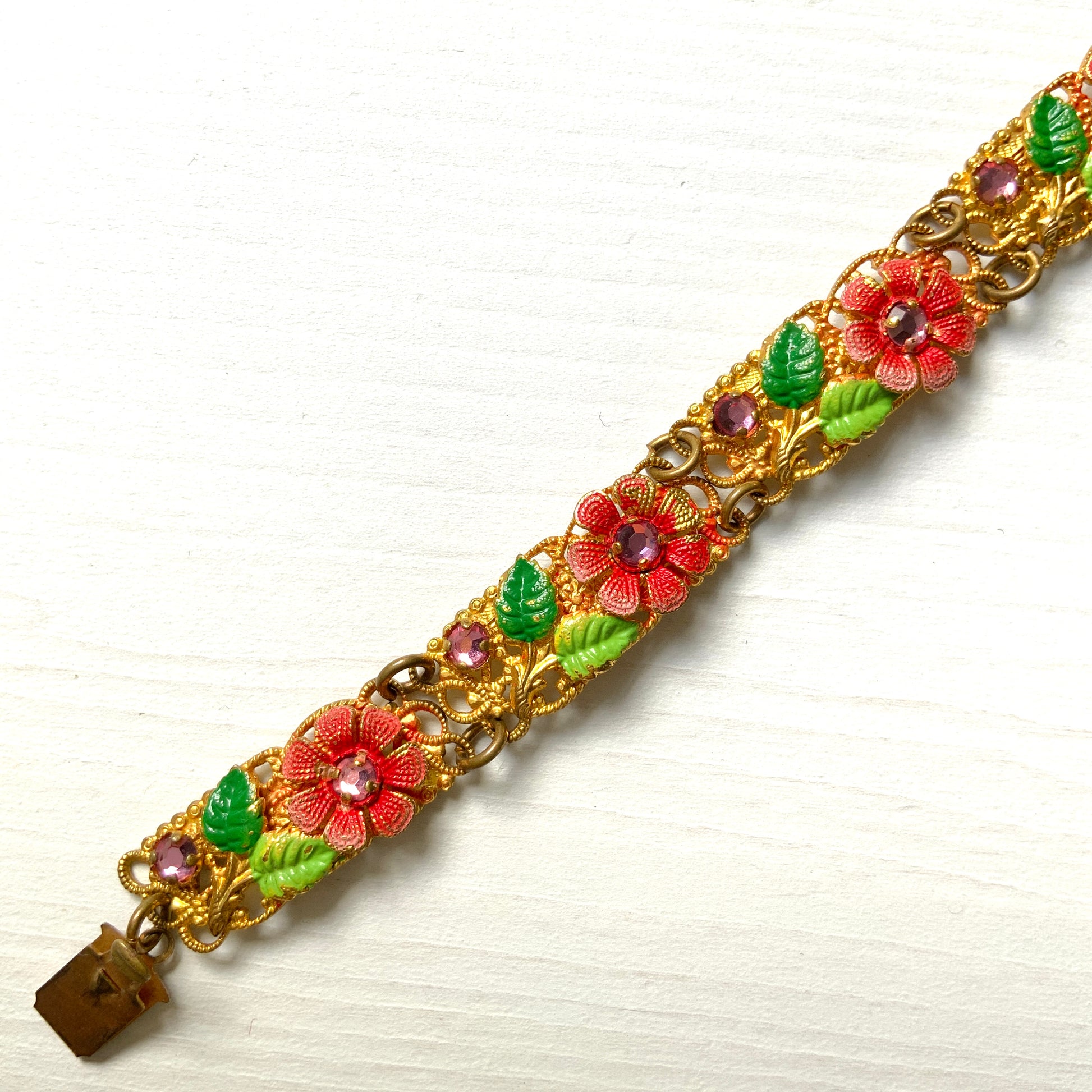 This gold-tone filigree bracelet features charming pink flowers delicately painted onto its dainty filigree plates. かわいらしいピンクのお花が描かれたゴールドトーンのフィリグリーのブレスレット。