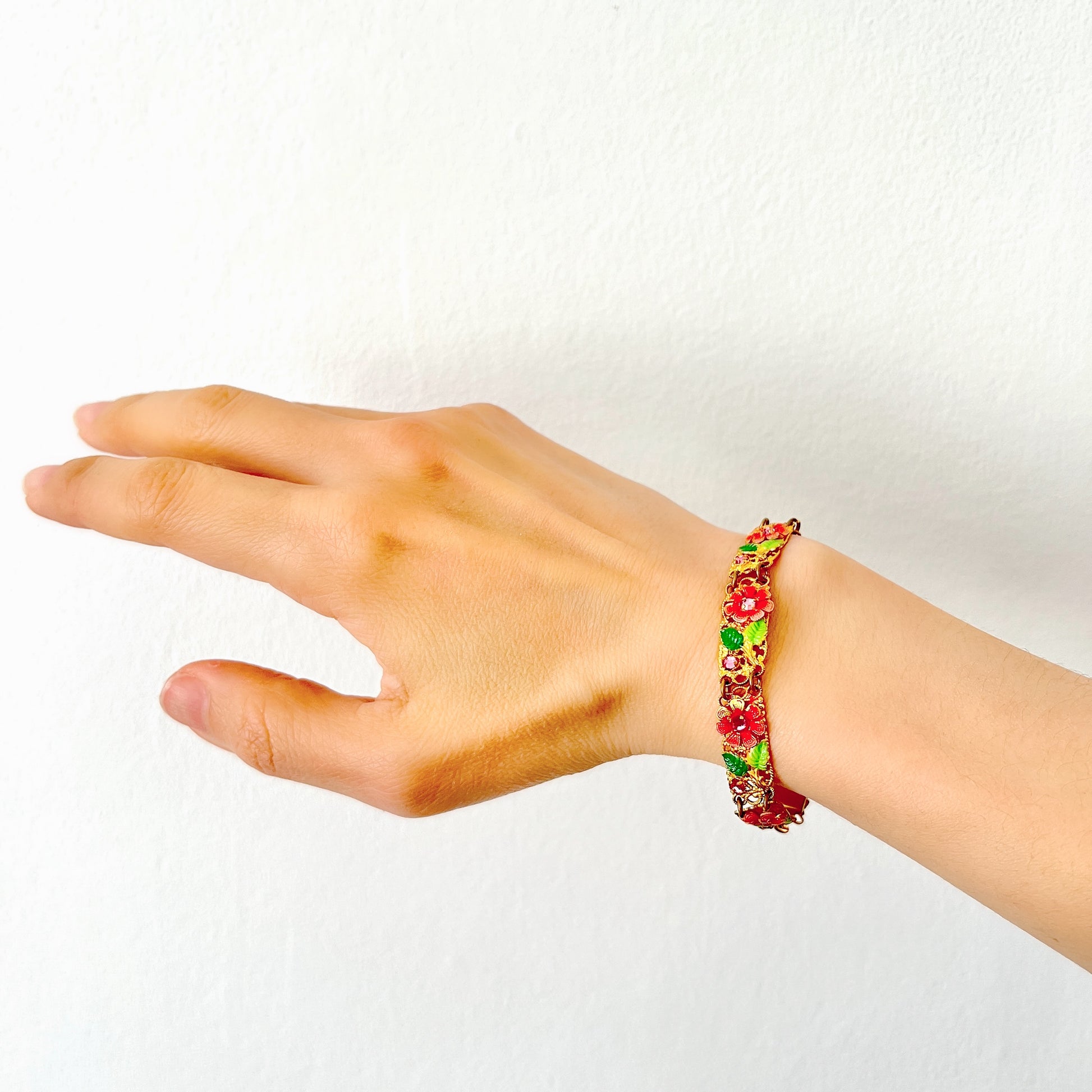 This gold-tone filigree bracelet features charming pink flowers delicately painted onto its dainty filigree plates. かわいらしいピンクのお花が描かれたゴールドトーンのフィリグリーのブレスレット。