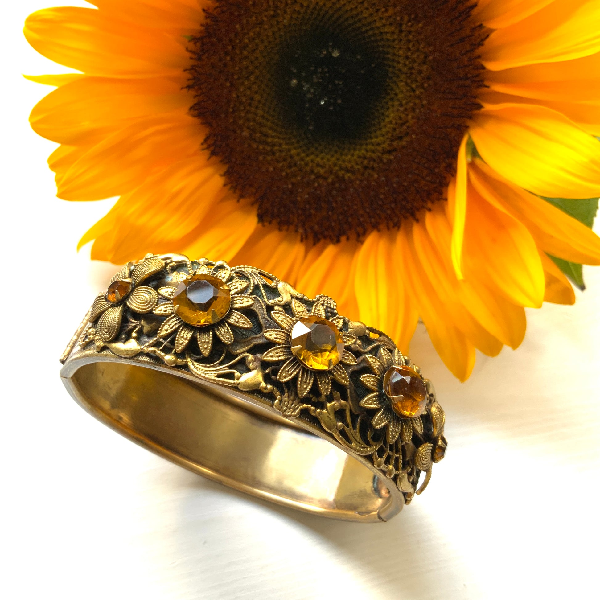 A decorative bangle featuring intricate floral motifs on gold-tone metal, with a filigree inspired design.  ゴールドトーンのメタルに、フィリグリー風の繊細な花模様があしらわれたデコラティブなバングル。