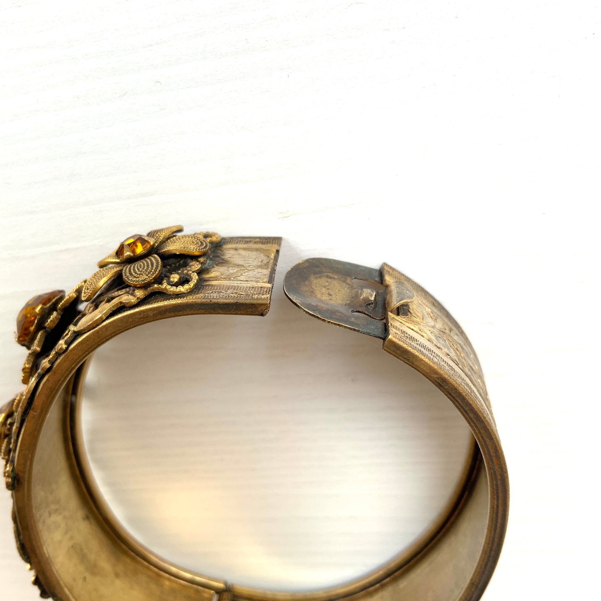 A decorative bangle featuring intricate floral motifs on gold-tone metal, with a filigree inspired design.  ゴールドトーンのメタルに、フィリグリー風の繊細な花模様があしらわれたデコラティブなバングル。