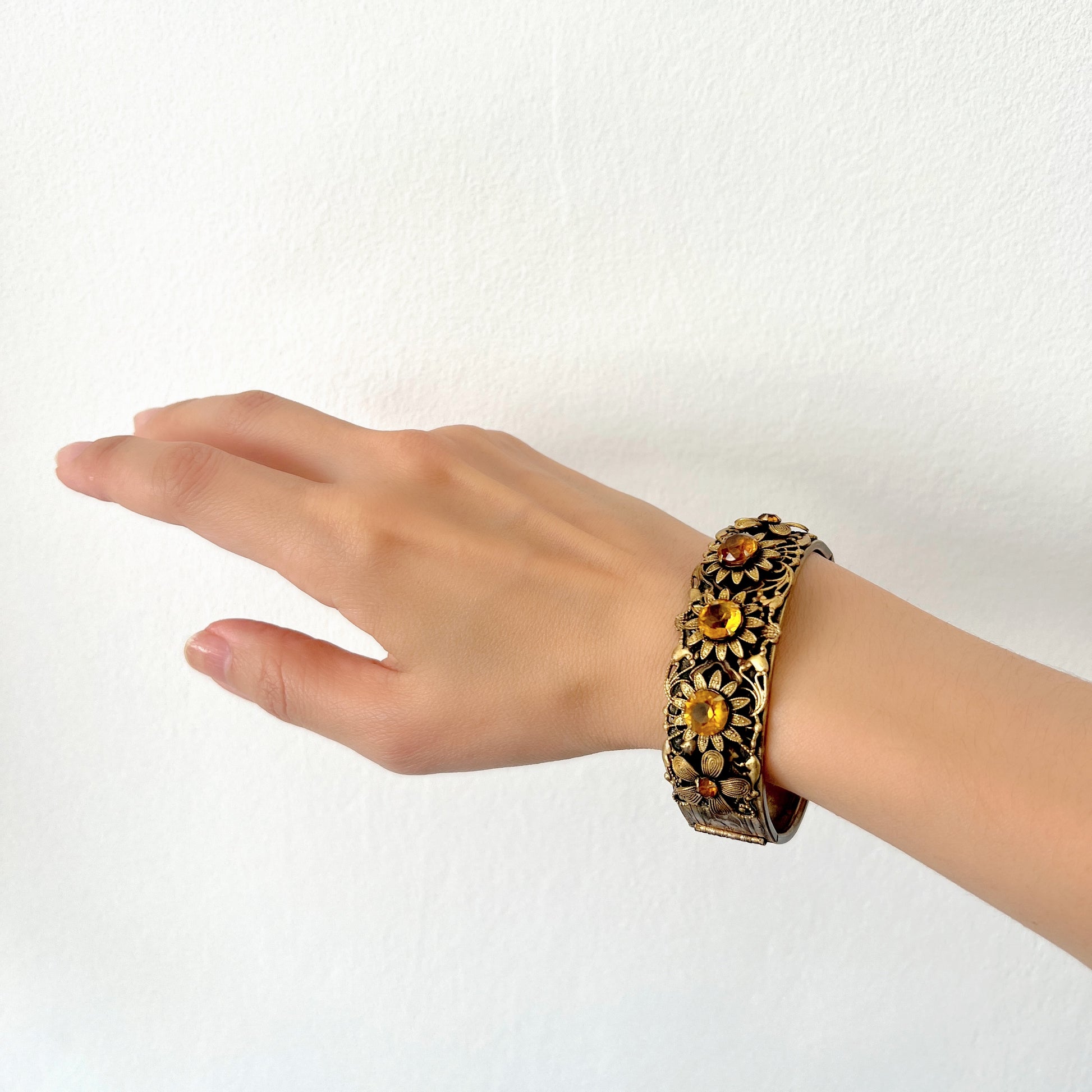 A decorative bangle featuring intricate floral motifs on gold-tone metal, with a filigree inspired design.  ゴールドトーンのメタルに、フィリグリー風の繊細な花模様があしらわれたデコラティブなバングル。