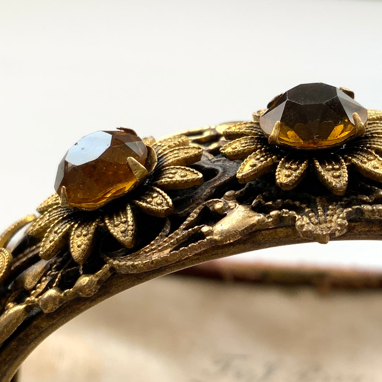 A decorative bangle featuring intricate floral motifs on gold-tone metal, with a filigree inspired design.  ゴールドトーンのメタルに、フィリグリー風の繊細な花模様があしらわれたデコラティブなバングル。