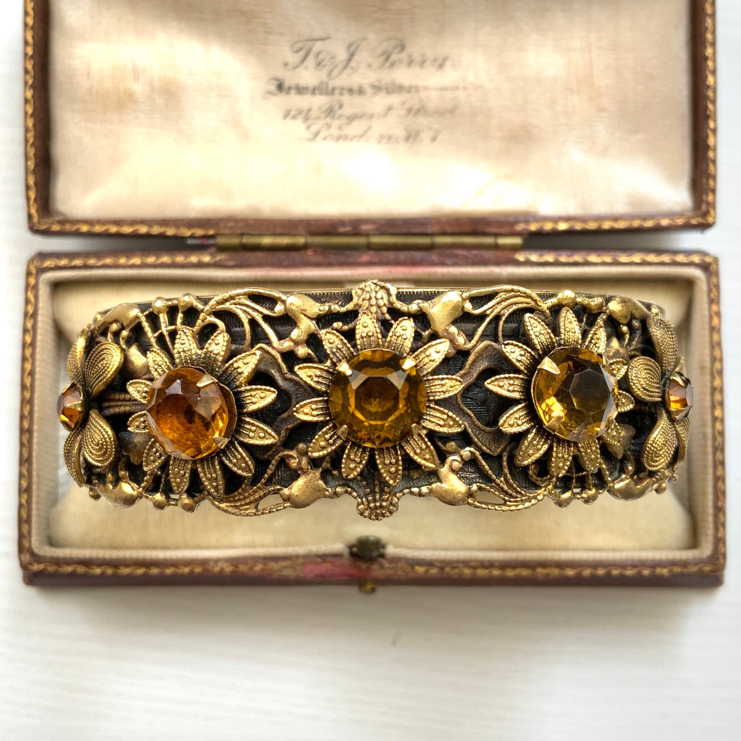 A decorative bangle featuring intricate floral motifs on gold-tone metal, with a filigree inspired design.  ゴールドトーンのメタルに、フィリグリー風の繊細な花模様があしらわれたデコラティブなバングル。