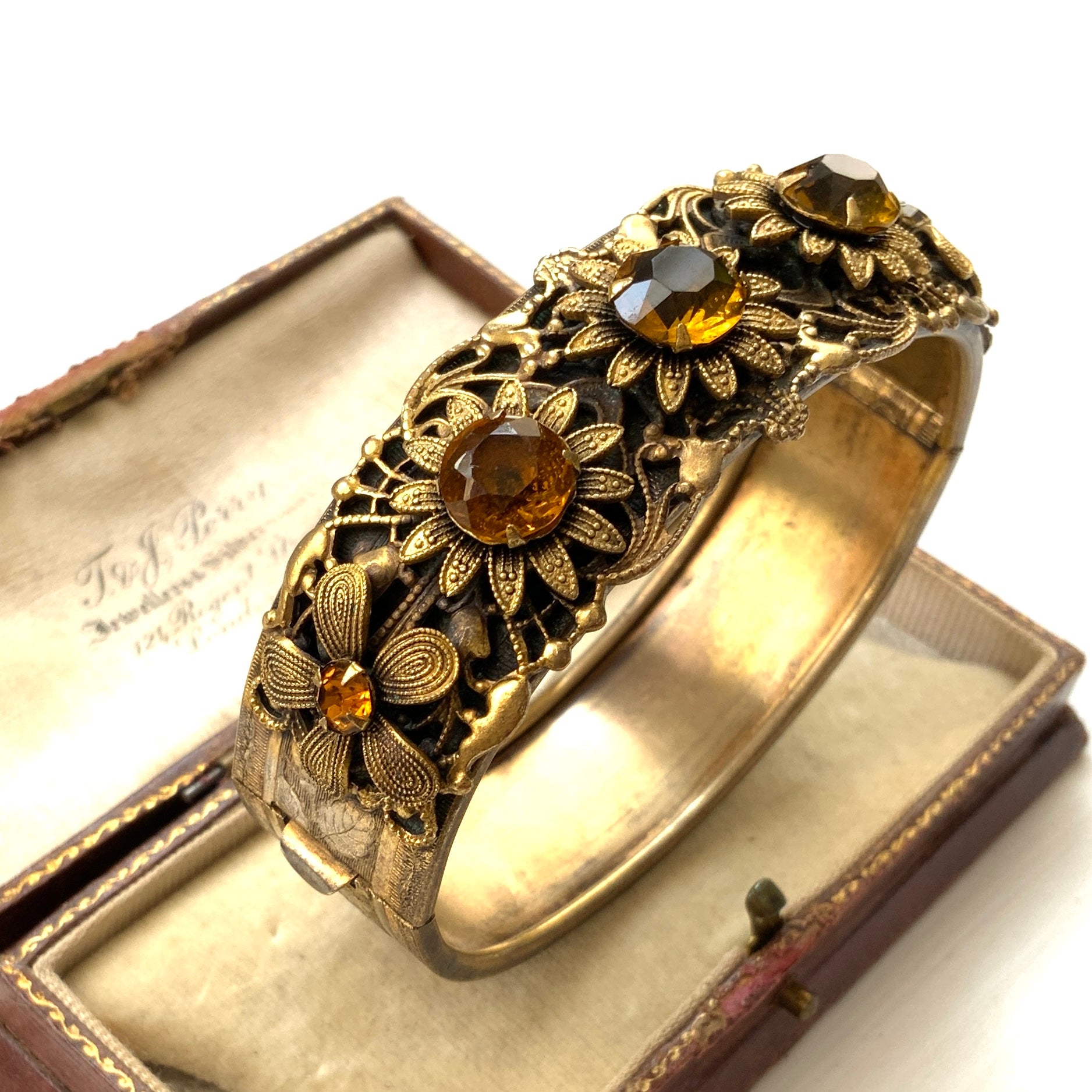 A decorative bangle featuring intricate floral motifs on gold-tone metal, with a filigree inspired design.  ゴールドトーンのメタルに、フィリグリー風の繊細な花模様があしらわれたデコラティブなバングル。