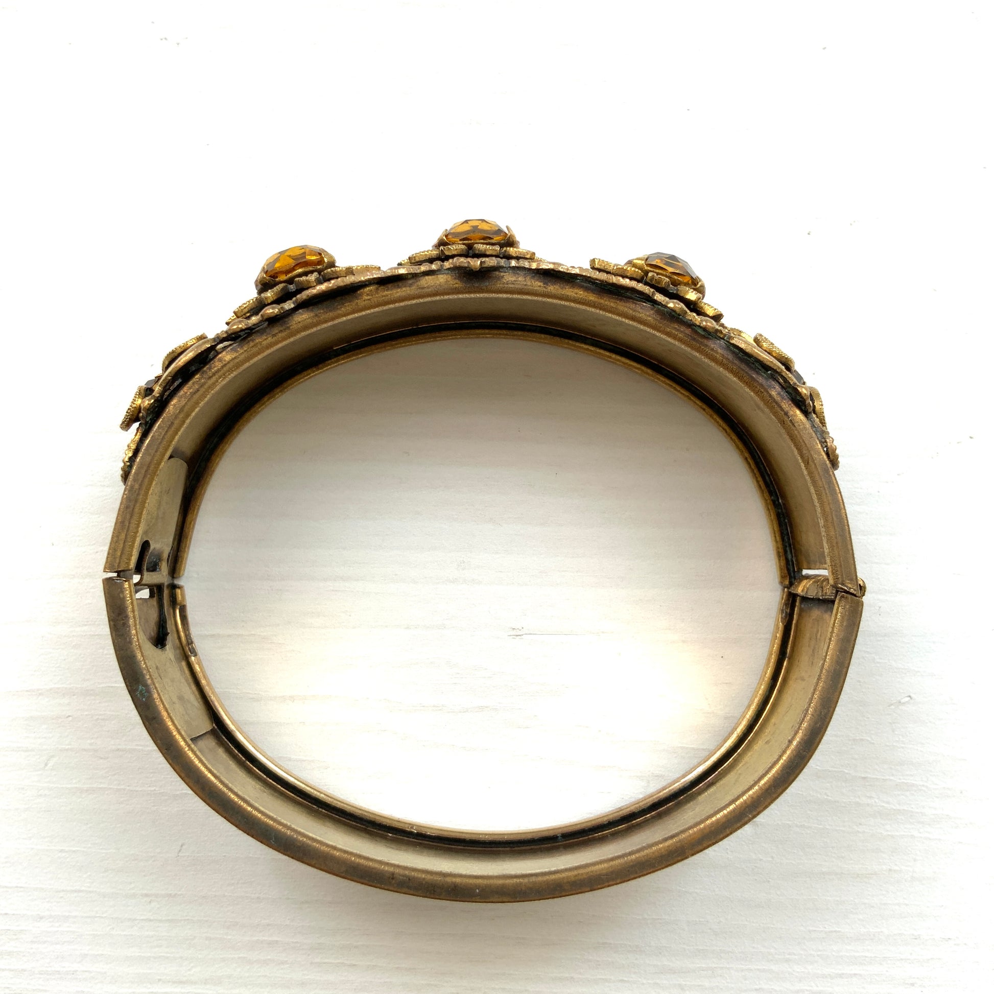 A decorative bangle featuring intricate floral motifs on gold-tone metal, with a filigree inspired design.  ゴールドトーンのメタルに、フィリグリー風の繊細な花模様があしらわれたデコラティブなバングル。