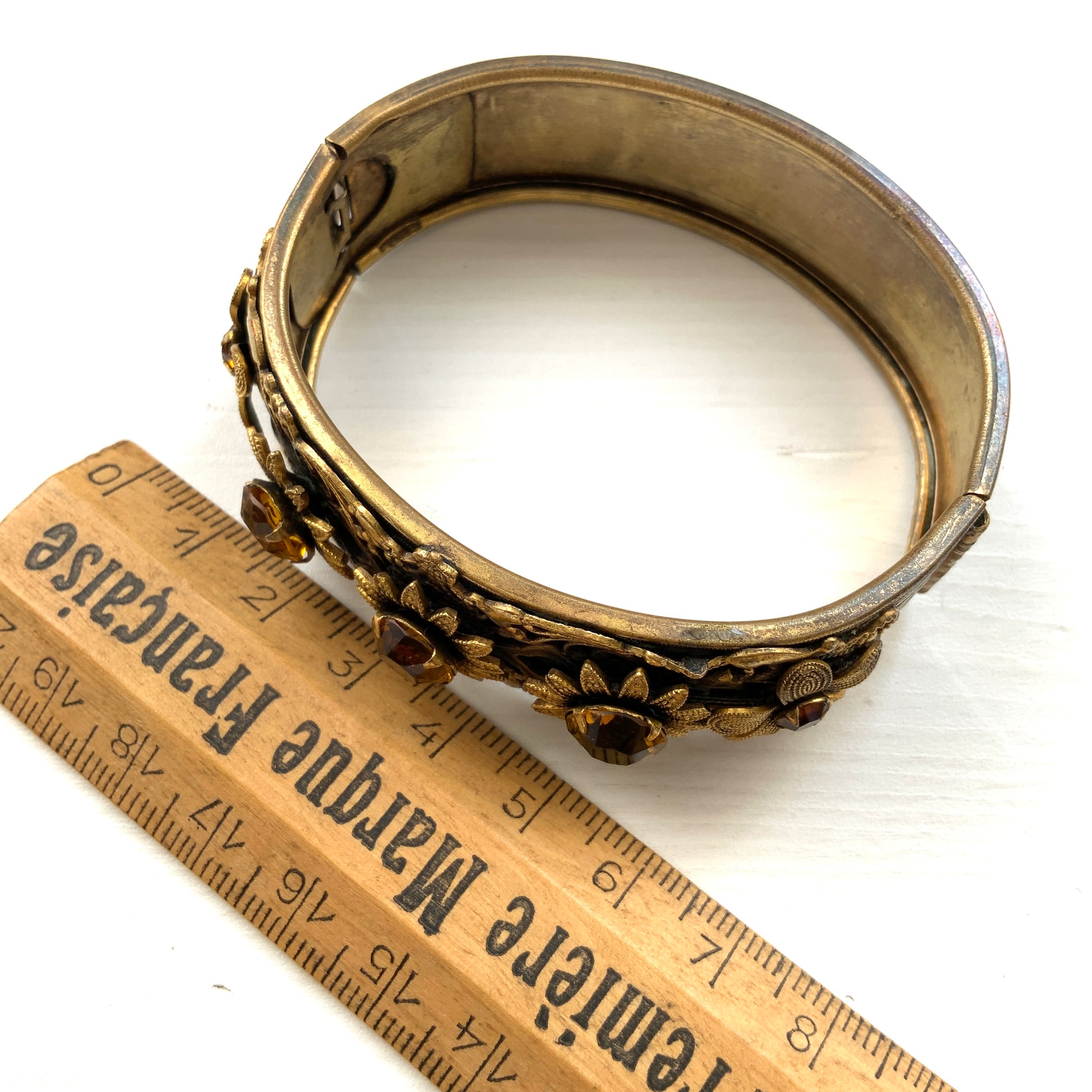 A decorative bangle featuring intricate floral motifs on gold-tone metal, with a filigree inspired design.  ゴールドトーンのメタルに、フィリグリー風の繊細な花模様があしらわれたデコラティブなバングル。