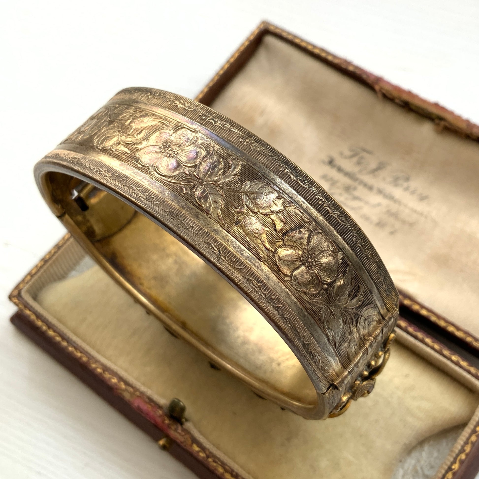 A decorative bangle featuring intricate floral motifs on gold-tone metal, with a filigree inspired design.  ゴールドトーンのメタルに、フィリグリー風の繊細な花模様があしらわれたデコラティブなバングル。