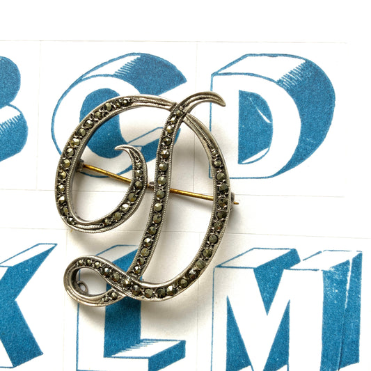  A silver brooch in the shape of the letter “D”, adorned with marcasites. マーカサイトが散りばめられた、シルバーの”D"のブローチ