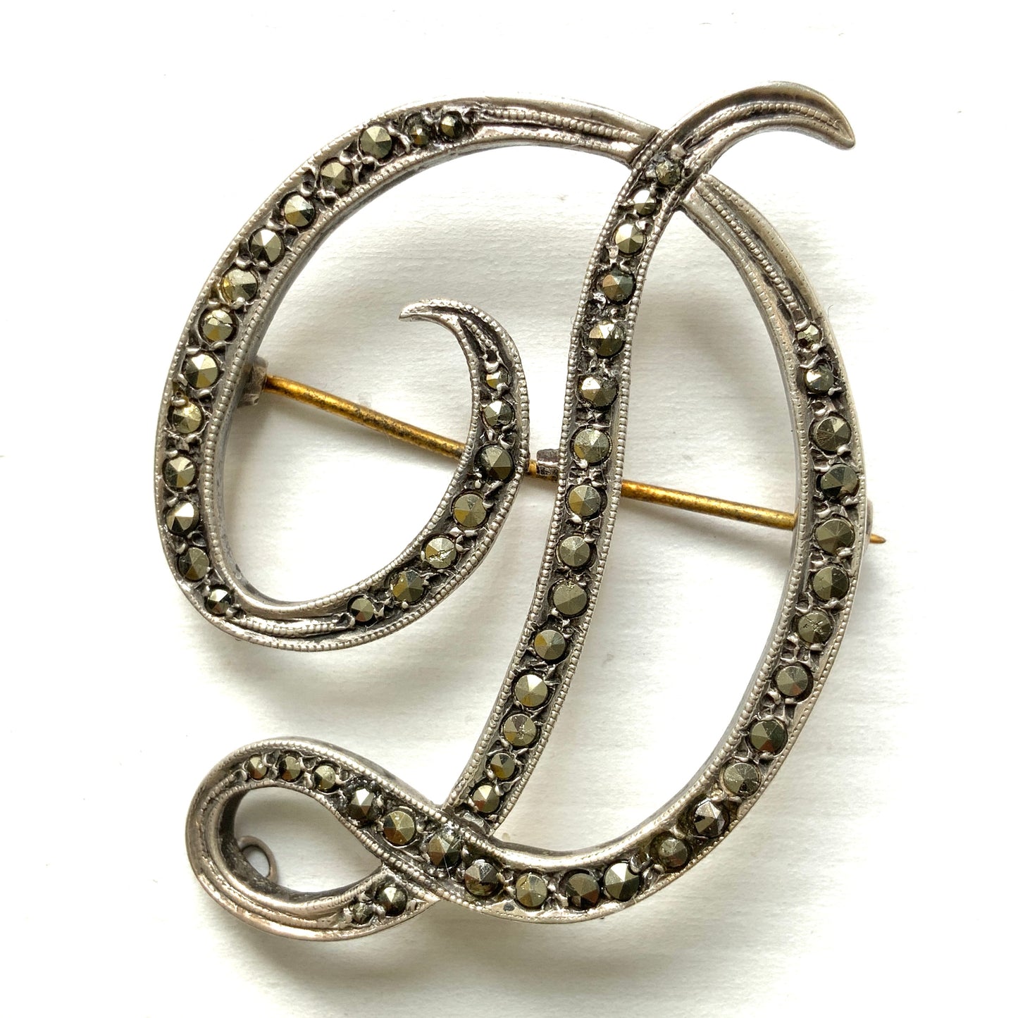  A silver brooch in the shape of the letter “D”, adorned with marcasites. マーカサイトが散りばめられた、シルバーの”D"のブローチ