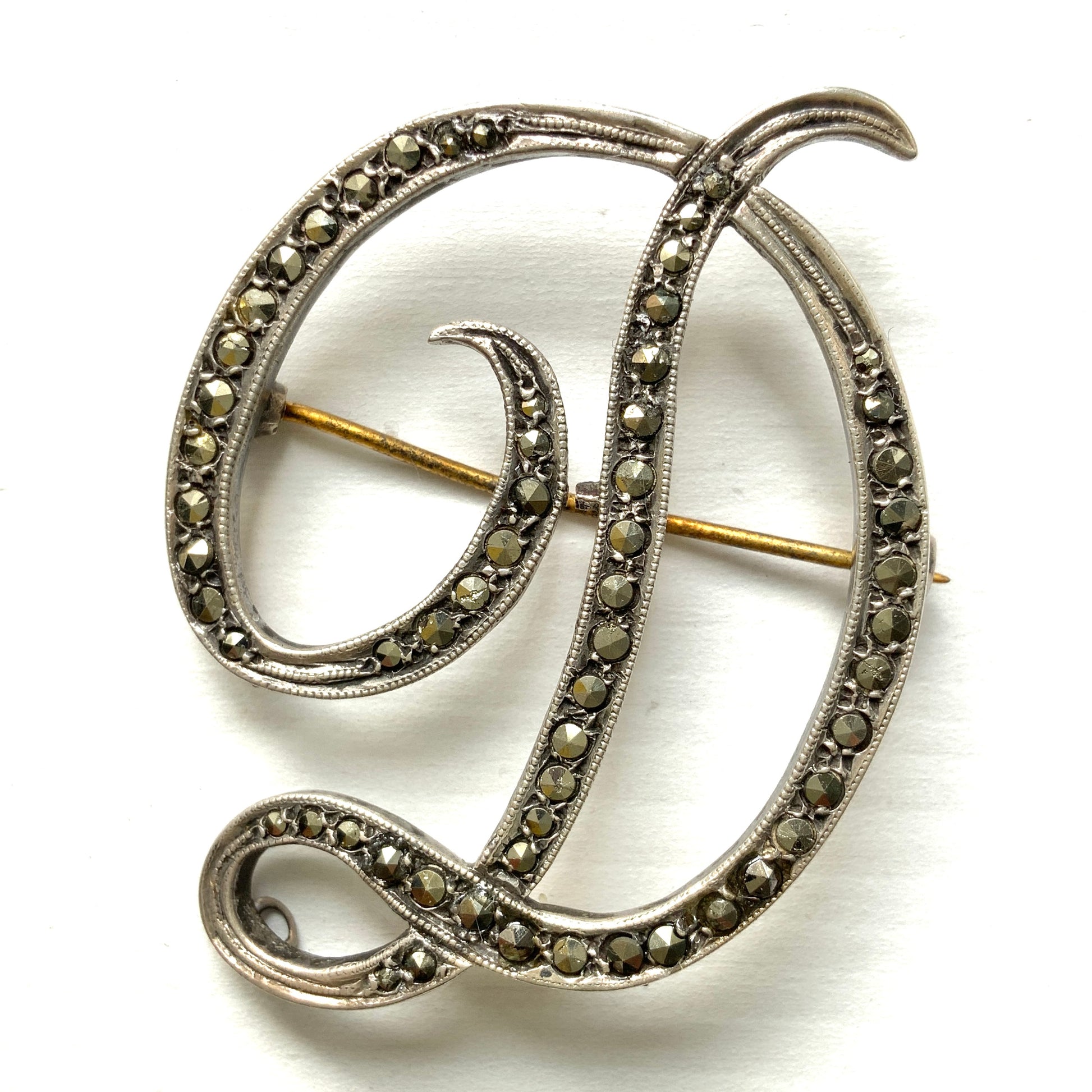  A silver brooch in the shape of the letter “D”, adorned with marcasites. マーカサイトが散りばめられた、シルバーの”D"のブローチ